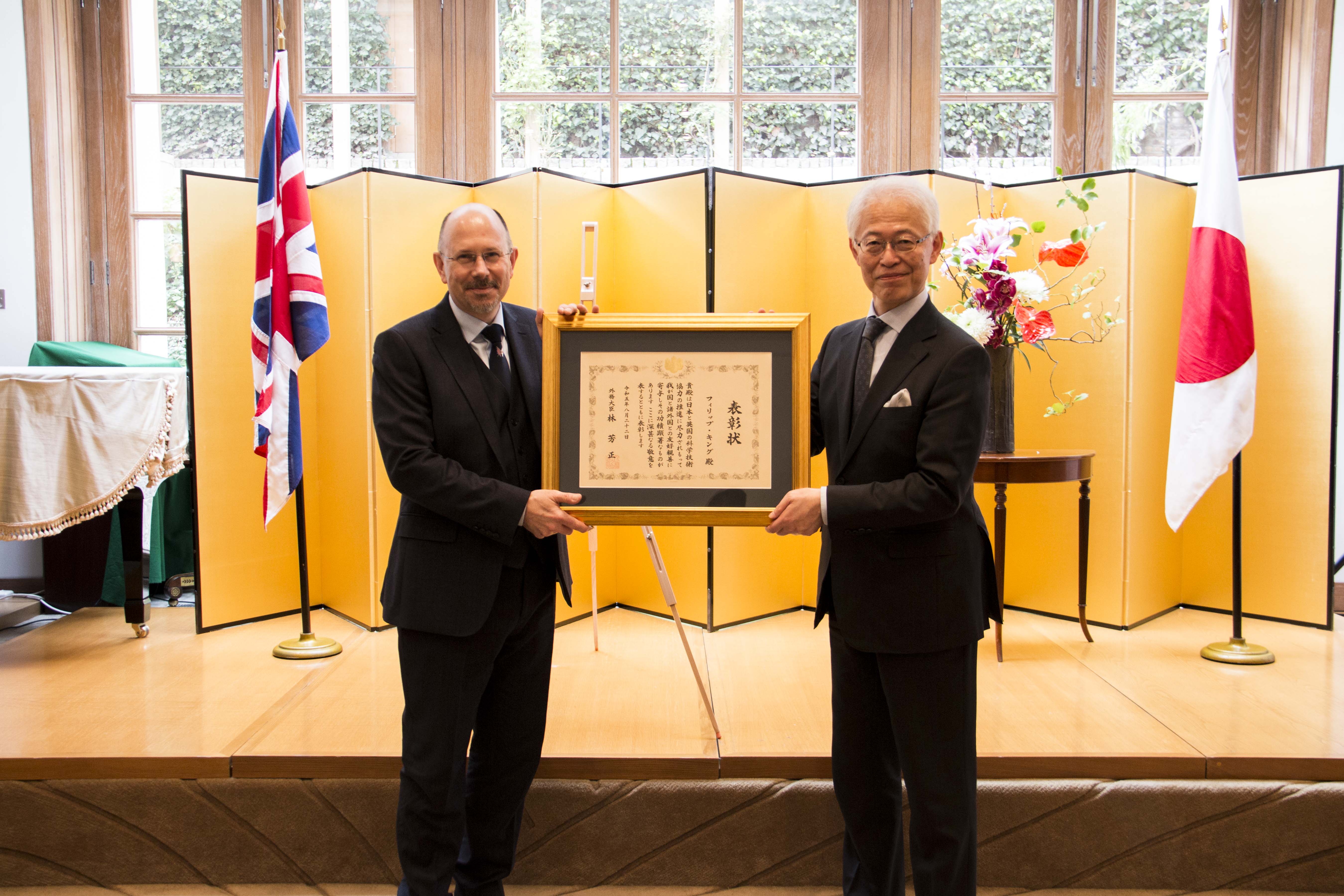 Philip King receives Foreign Minister's Commendation from Japanese Ambassador.the UK. The award is presented in a gold frame.