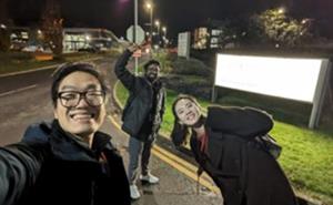 Three people smiling in front of a bright white sign