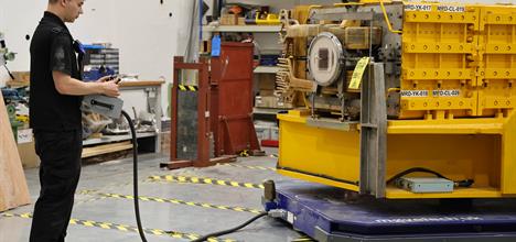 A man uses a control panel to move a large yellow magnet on a blue plate