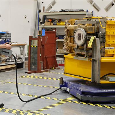 A man uses a control panel to move a large yellow magnet on a blue plate