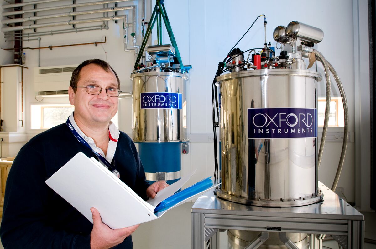 A man with an open folder stood next to some large dewars